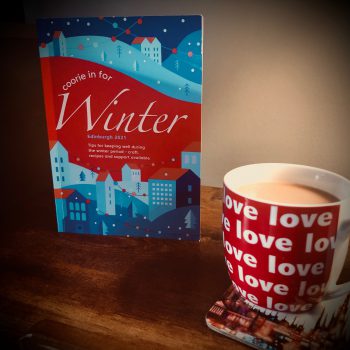 A photo of a mug of tea alongside a copy of the 'Coorie in for Winter' booklet