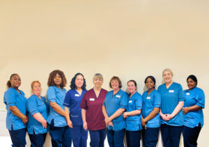 Image shows a group of nurses in blue uniforms in a row smiling