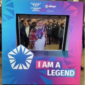 John in front of sign of Commonwealth Games